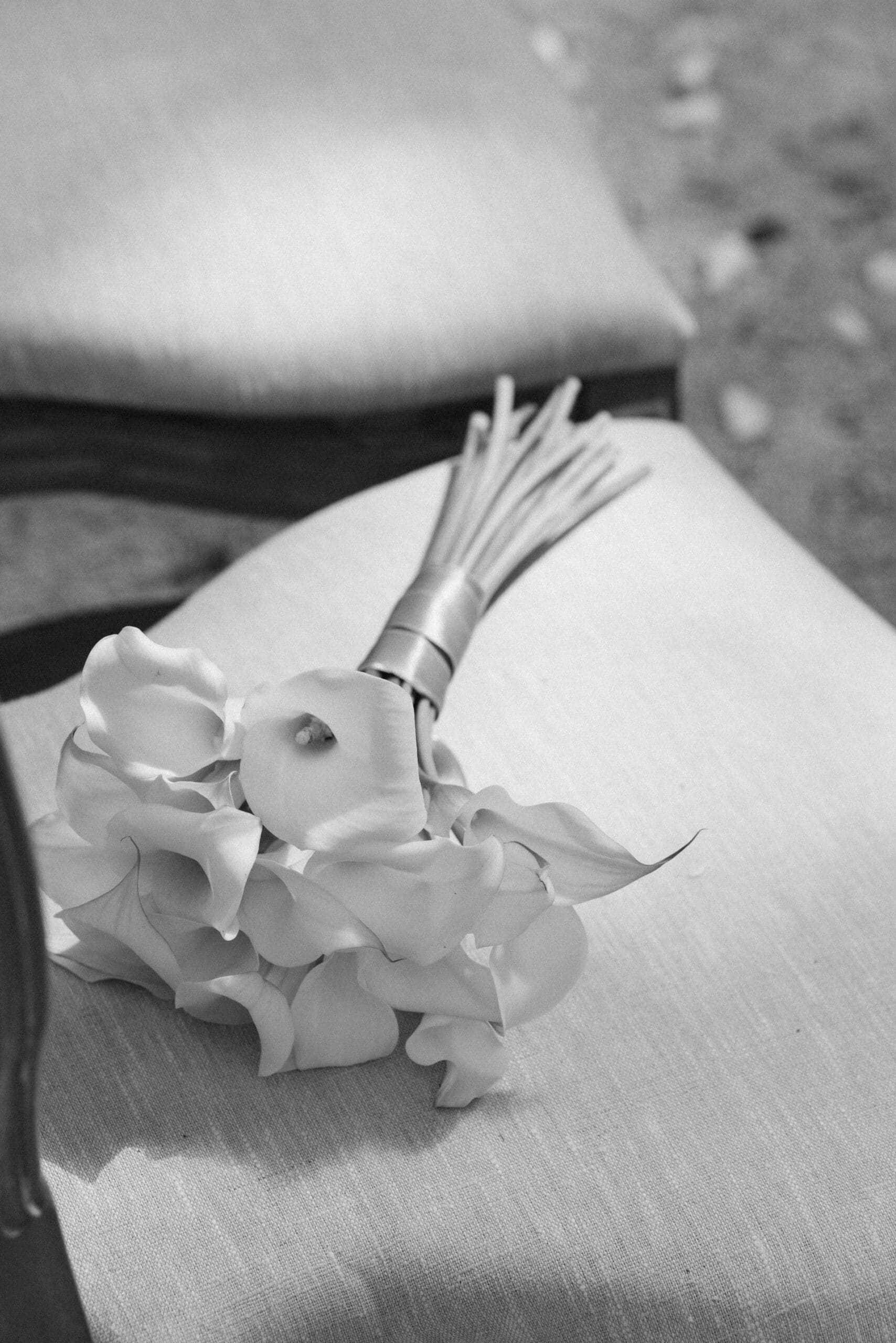 Élégant bouquet de mariage de Calla (Arums) aux pétales soyeux, les tiges nouées sur un coussin en lin, en noir et blanc.