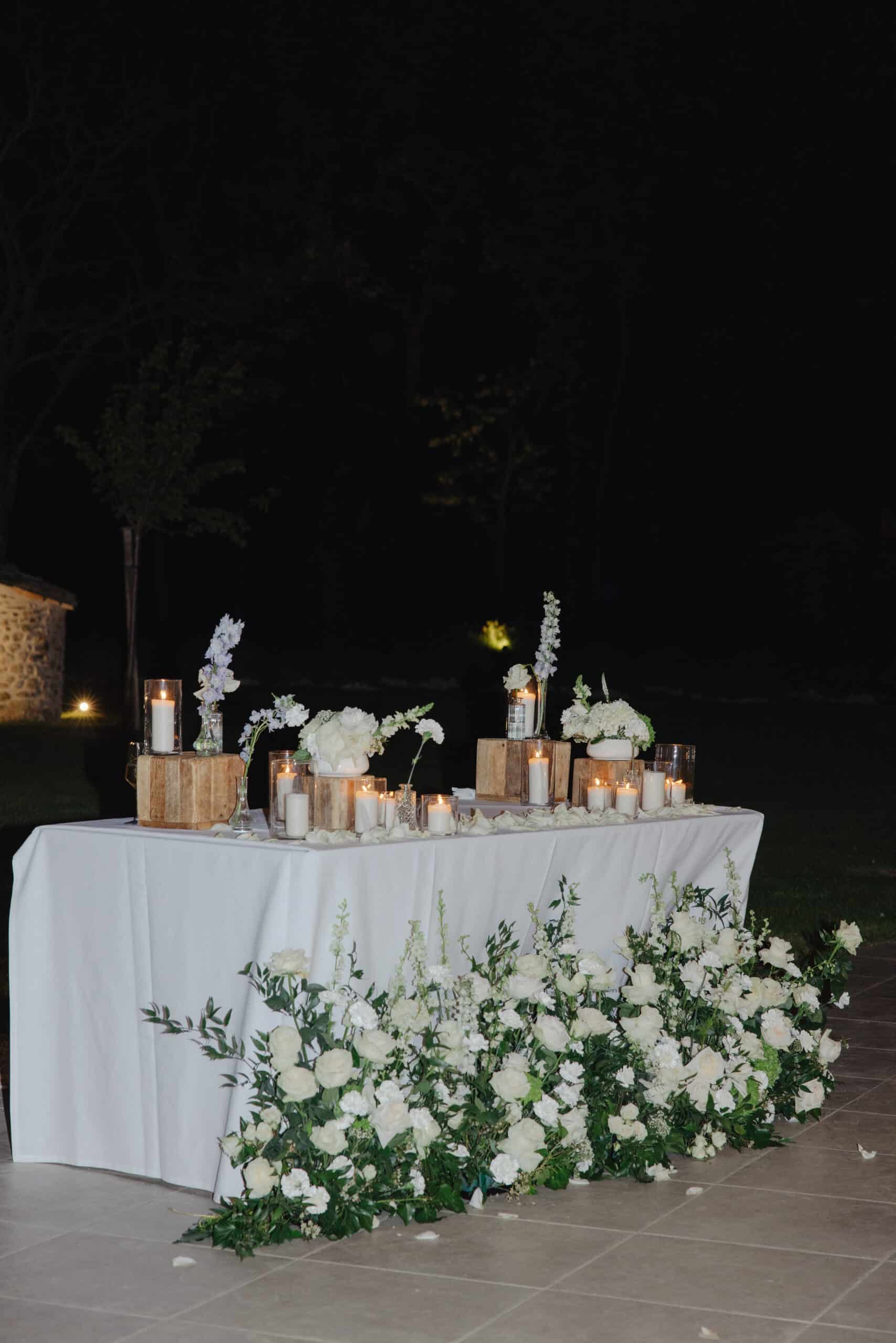 Magnifique décoration de table de mariage en soirée. Nappe blanche, bougies allumées, blocs de bois rustiques et opulents arrangements de roses blanches.
