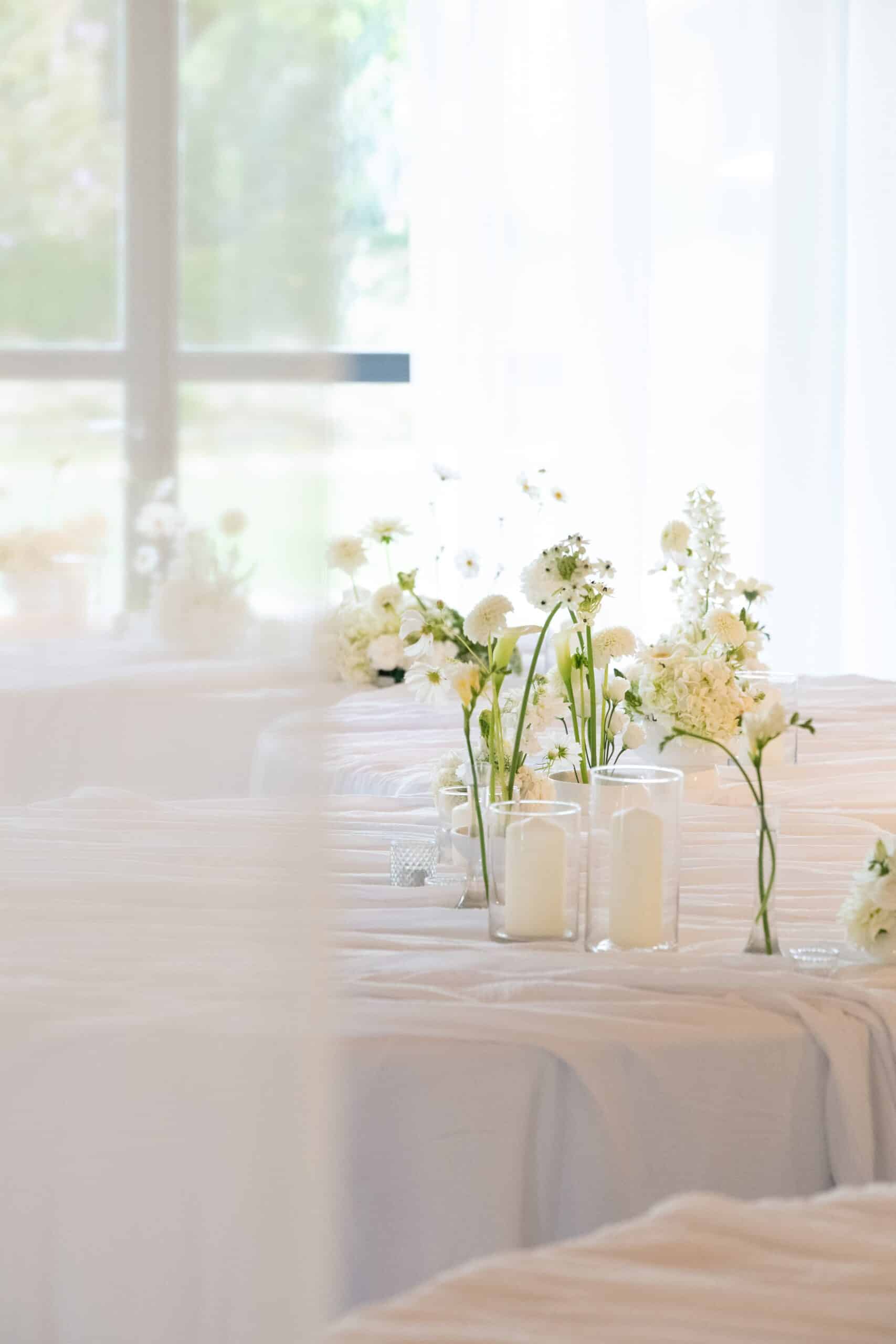 Élégante décoration de mariage minimaliste. Centres de table blancs: fleurs fraîches et bougies dans des vases en verre, lumière naturelle douce.