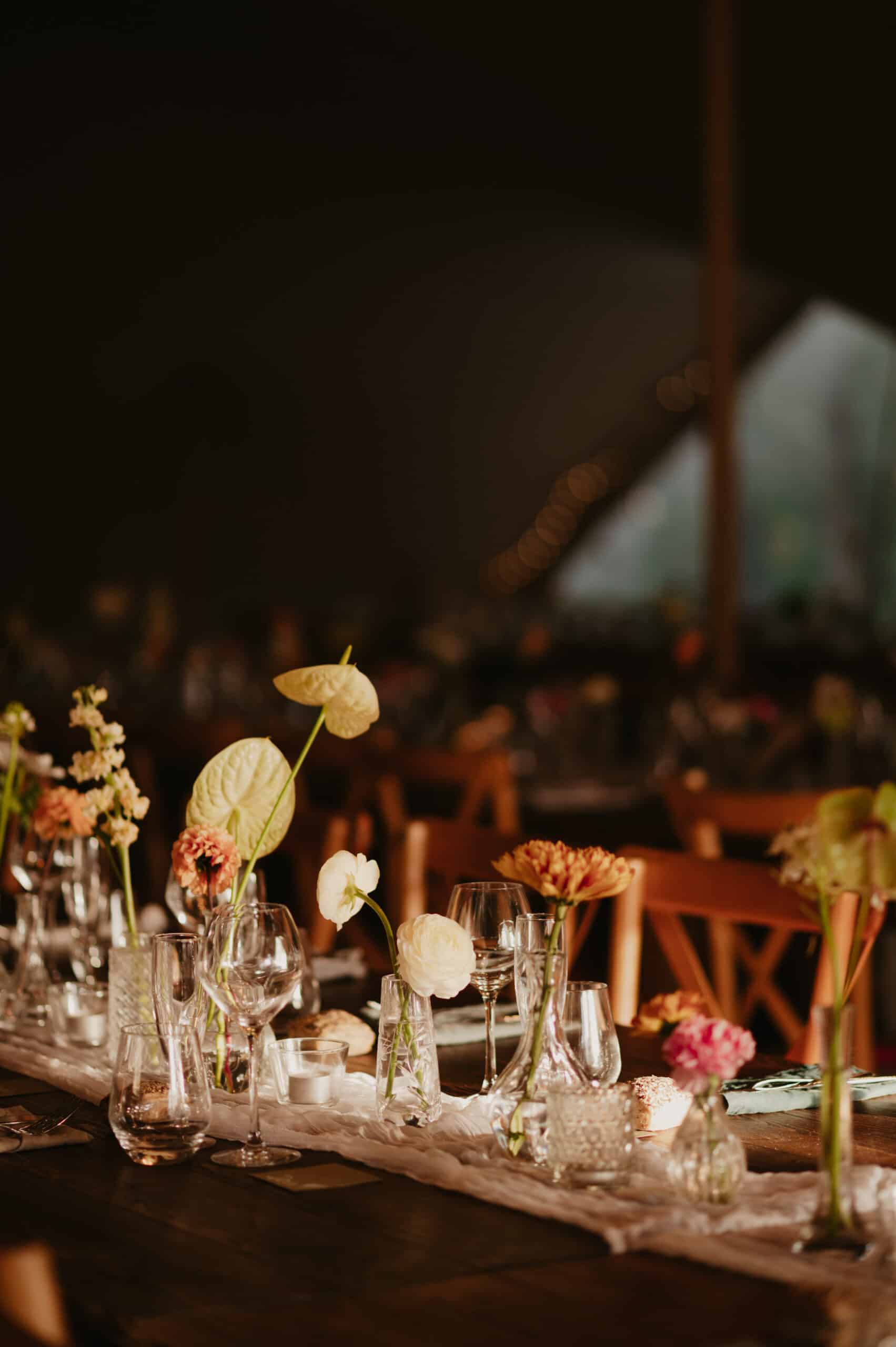 Décoration de table élégante pour un événement intime : renoncules, anthuriums et bougies sur un chemin de table vaporeux. Lumière chaleureuse.