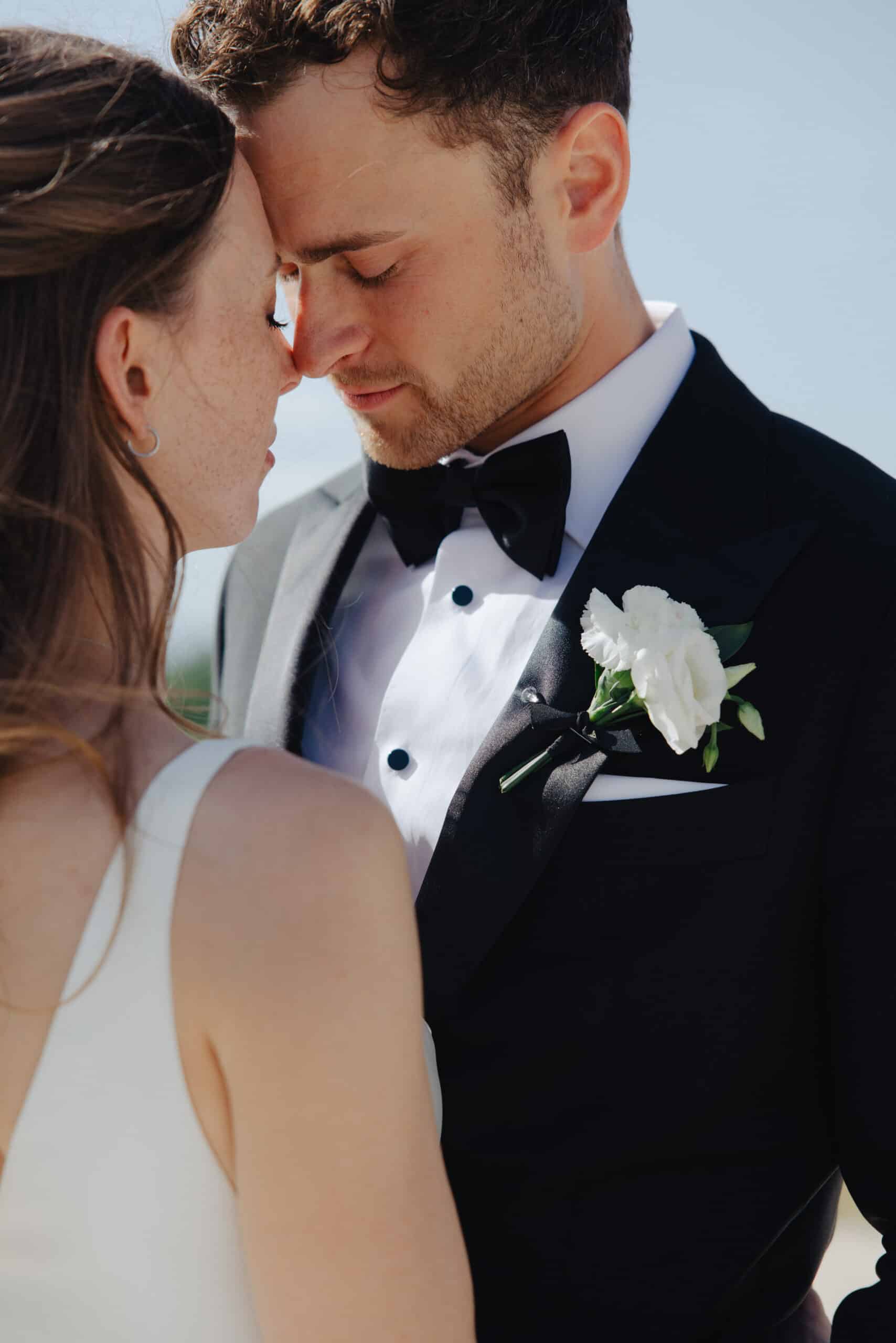 Gros plan intime de mariés, fronts contre fronts. Le marié en smoking noir et la mariée en robe blanche affichent une grande tendresse.