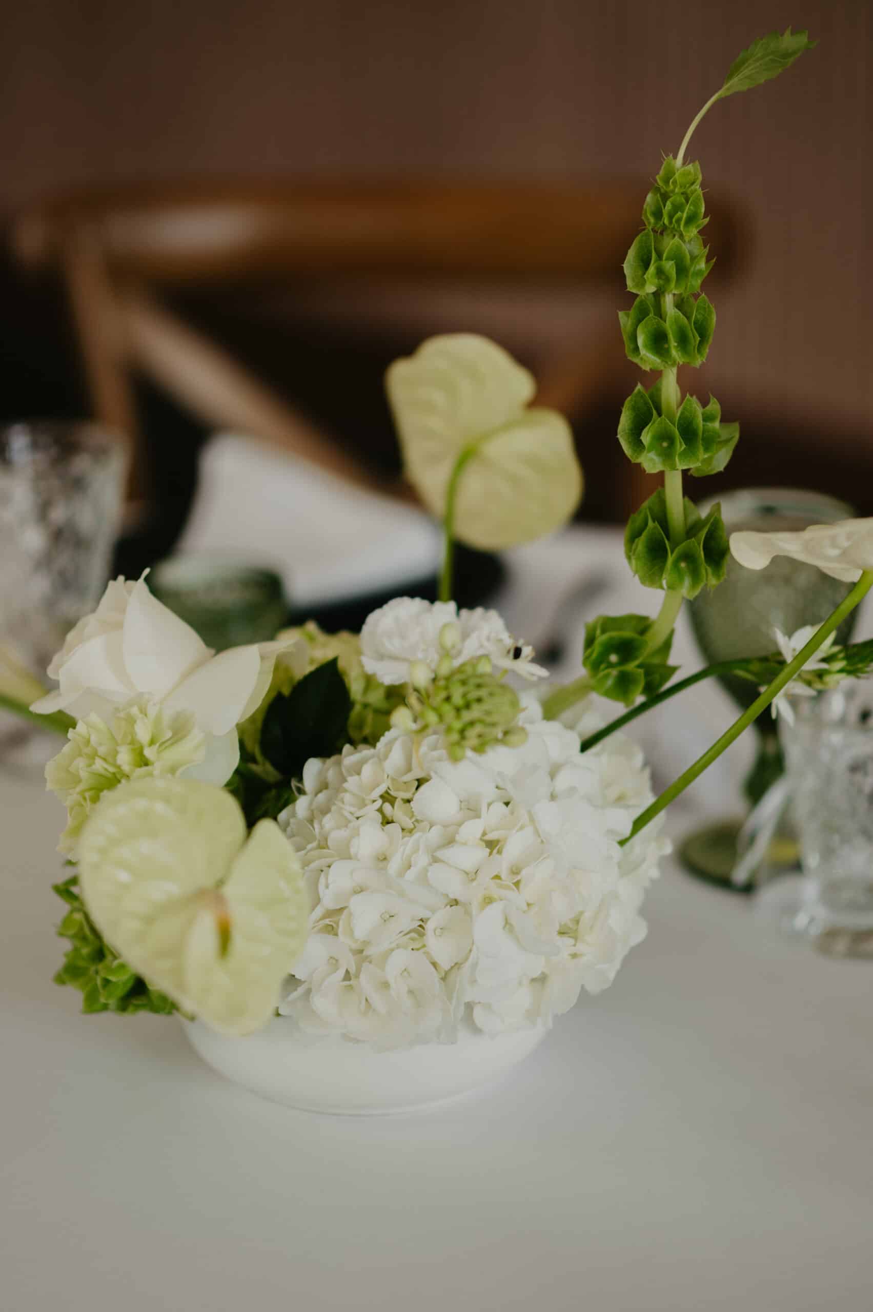 Composition florale blanche et vert sur table de réception. Hortensias, anthuriums et Moluccella dressent un décor élégant.