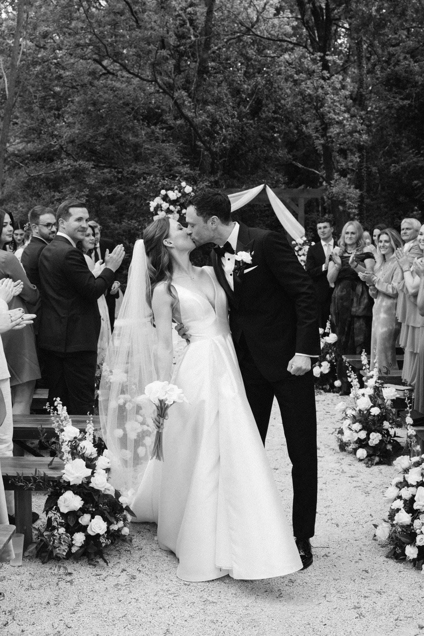 Premier baiser passionné des mariés en extérieur. Les invités applaudissent le couple célébrant leur union.