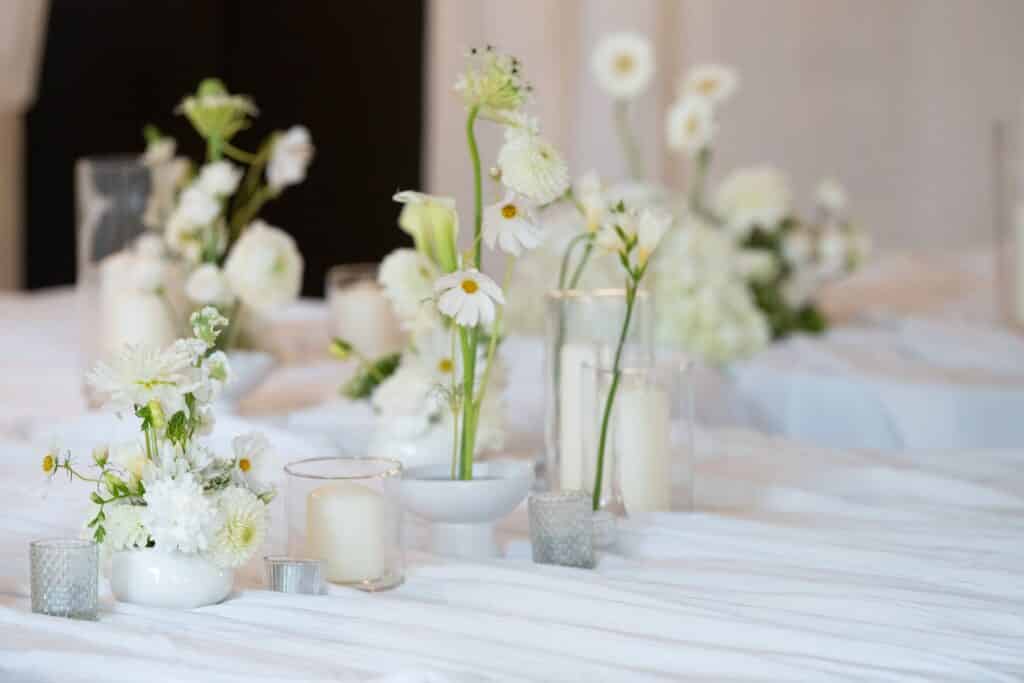 Centre de table mariage élégant : fleurs blanches et bougies Centre de table de mariage élégant avec fleurs blanches et bougies dans des vases minimalistes sur nappe blanche.